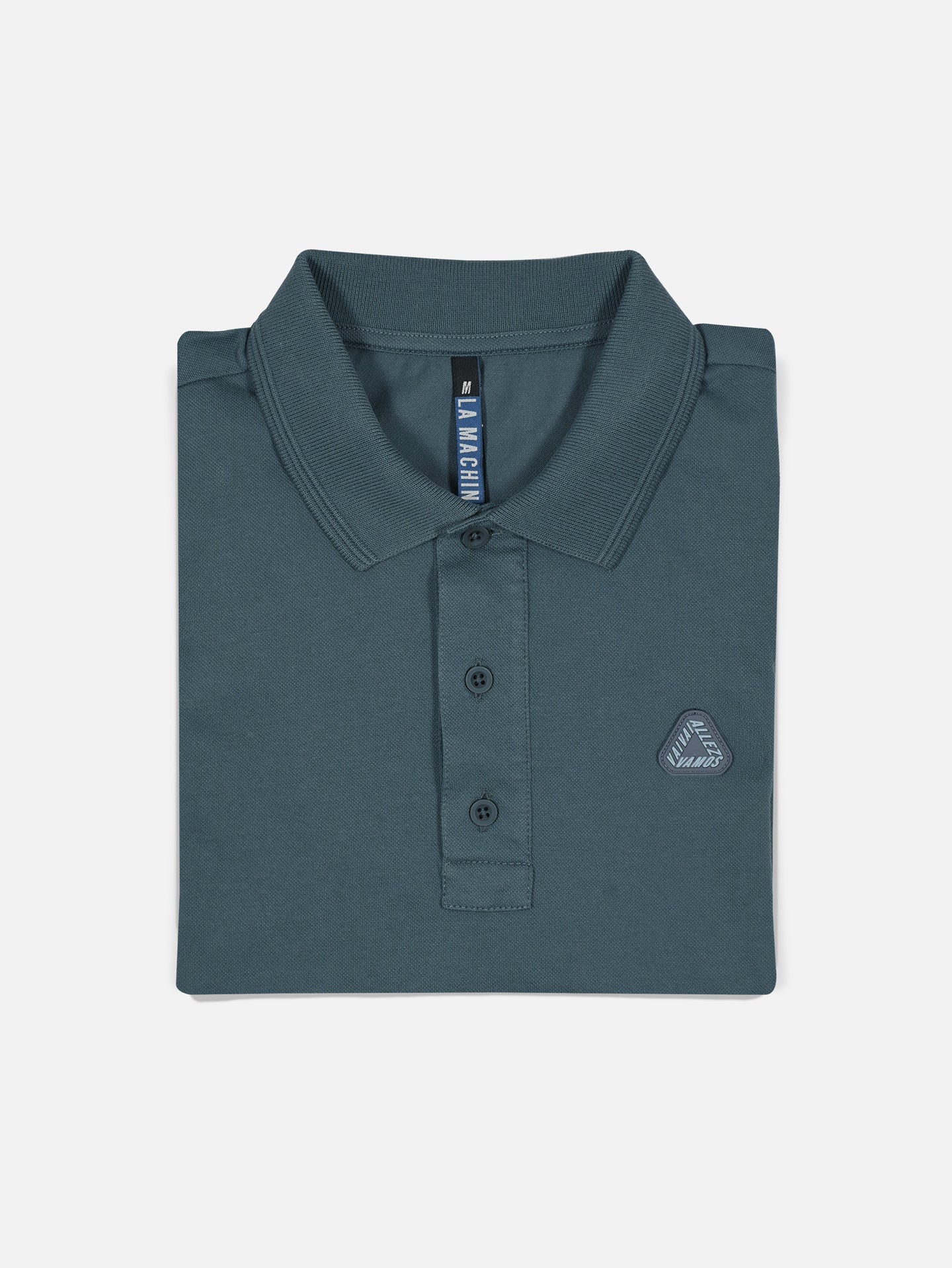 The Vai Allez Vamos Polo Shirt in Orion Blue by La Machine Cycle Club features a collar, three buttons, and a small embroidered logo on the left chest, neatly folded and displayed on a plain white background.