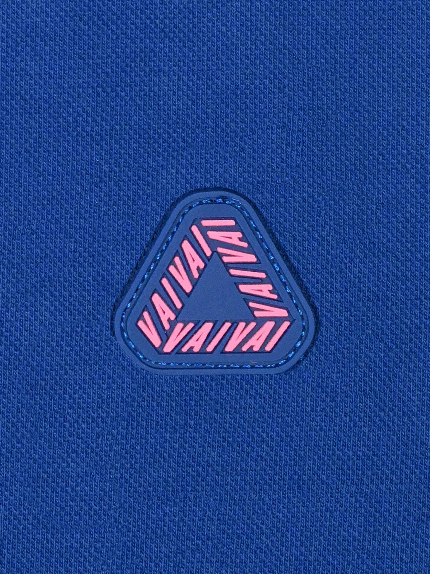 The La Machine Cycle Club Vai Vai - Giro d’Italia Polo shirt in Azzurra blue features textured fabric with a central triangle patch bordered in blue and pink VAI VAI text repeating along each side, reminiscent of cycling shirts.