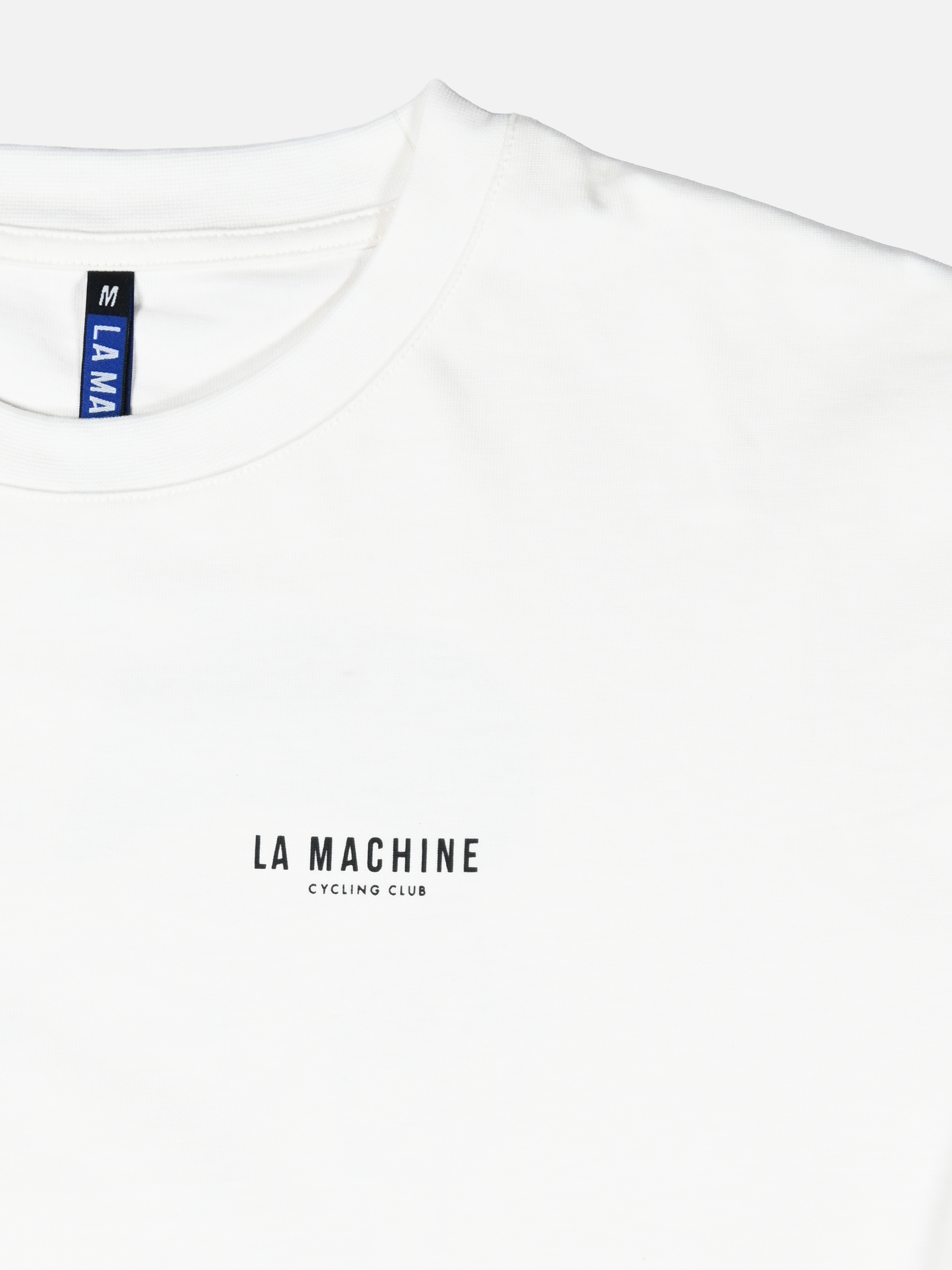 A white La Machine Cycle Club Directeur Sportif longsleeve with small black chest print, featuring LA MA and size M on the tag—a staple for any cycling culture shirt collection.