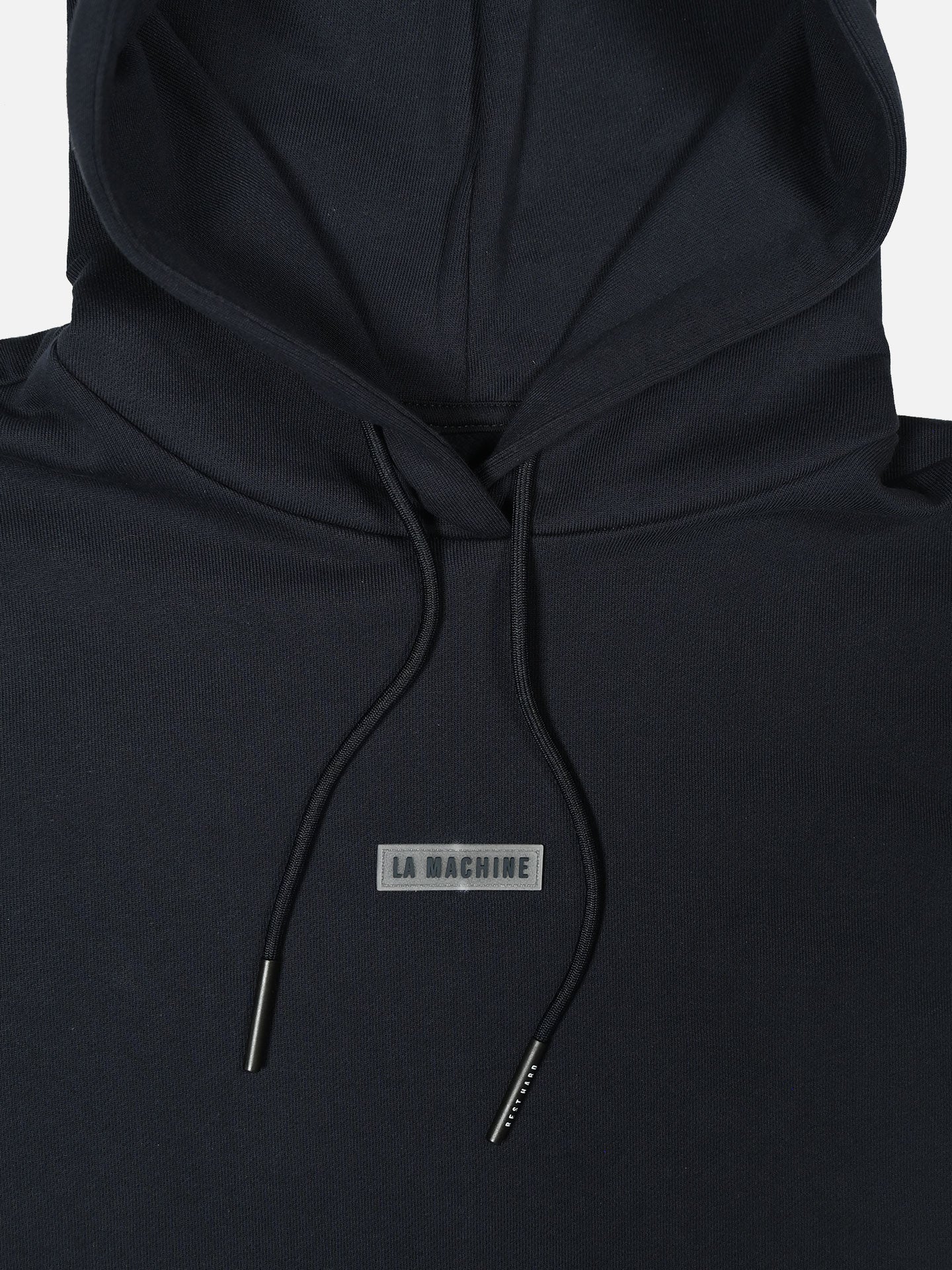 Close-up of the Ride Hard Rest Hard - Hoodie by La Machine Cycle Club, a unisex black sweatshirt with hood, drawstrings, and a chest patch reading LA MACHINE in gray. Made from 100% cotton for comfort and style.
