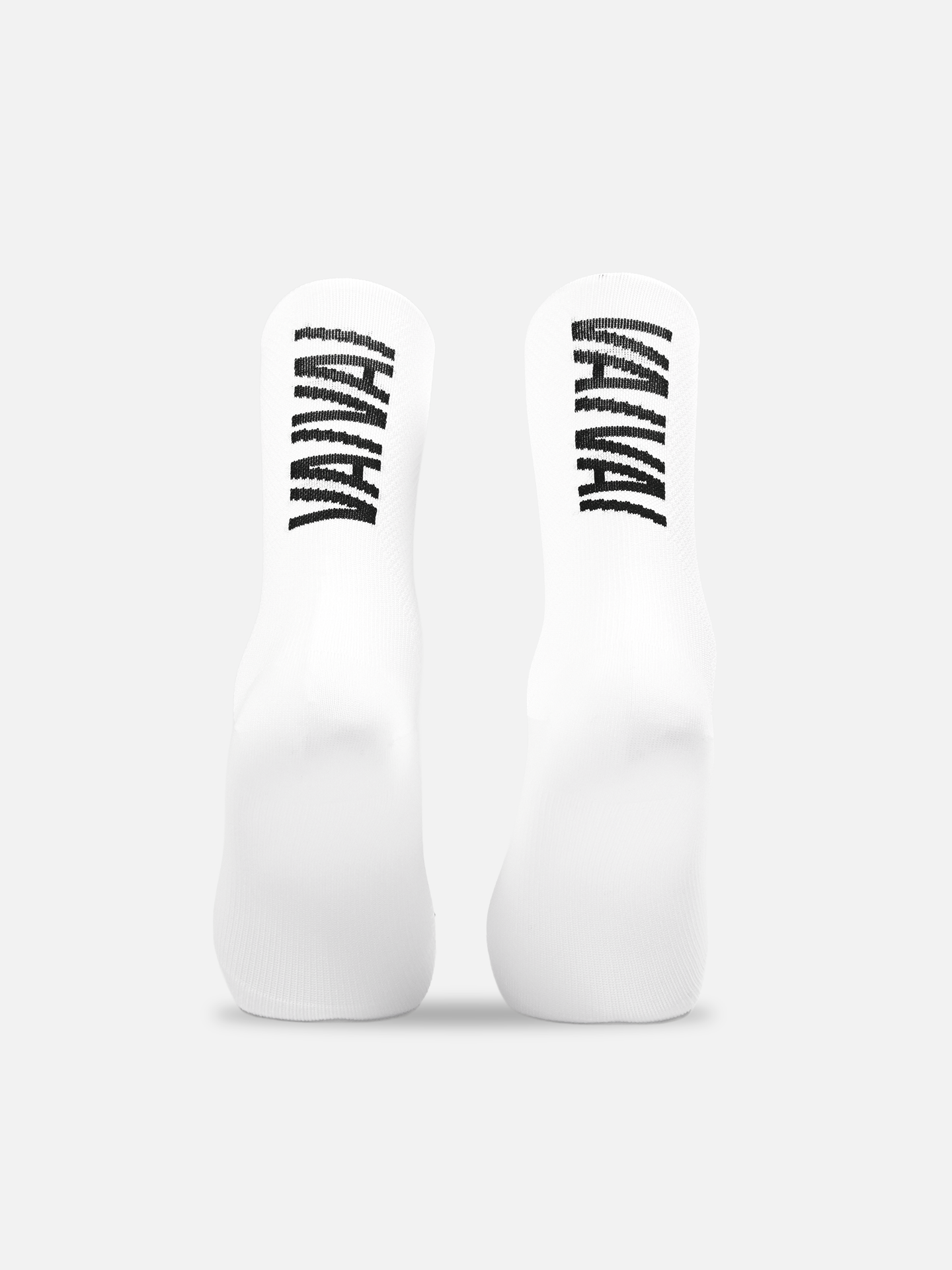 La Machine Cycle Club’s Vai Vai Cycling Socks are shown upright, all-white with black abstract vertical stripes on the soles, set against a plain light gray background. They feature a seamless toe for extra comfort.
