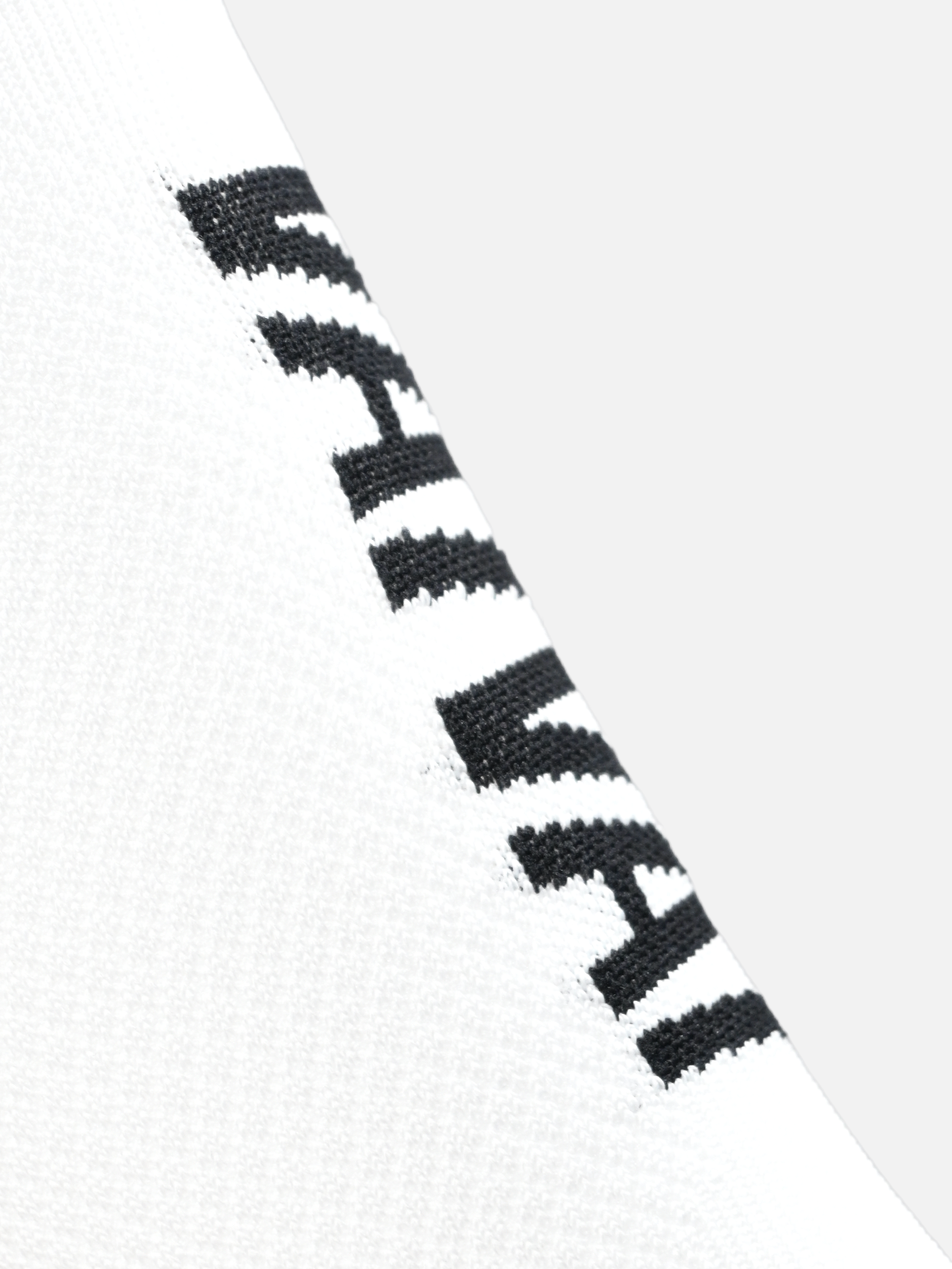 Close-up of the Vai Vai - Cycling Socks by La Machine Cycle Club, featuring an all-white design with bold black woven text running diagonally. The seamless toe offers enhanced comfort against a plain light gray background.