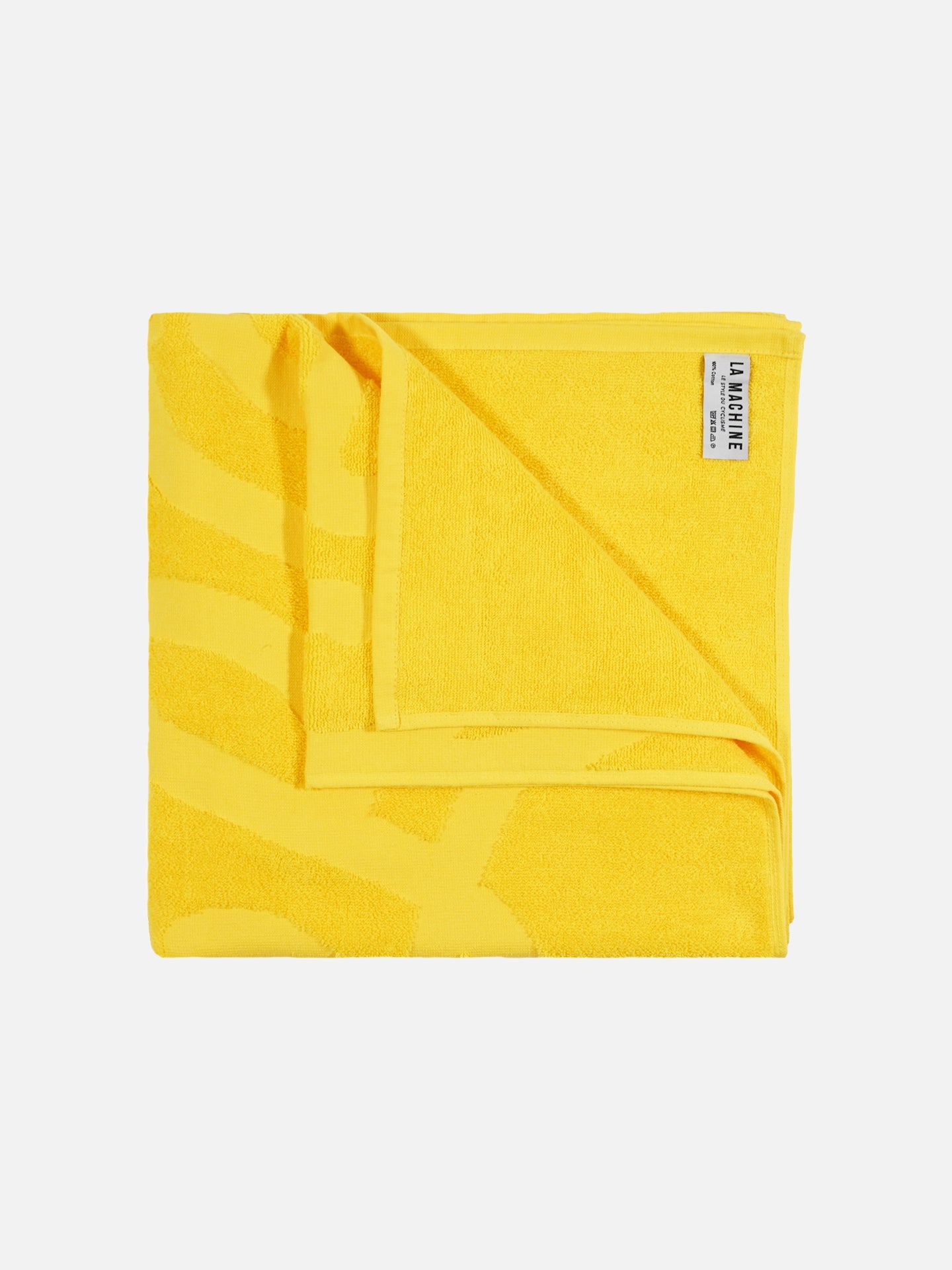 A folded yellow Le Tour de la Plage beach towel by La Machine Cycle Club, featuring a subtle pattern and a white label with the brand name in the top right corner, set against a plain white background.