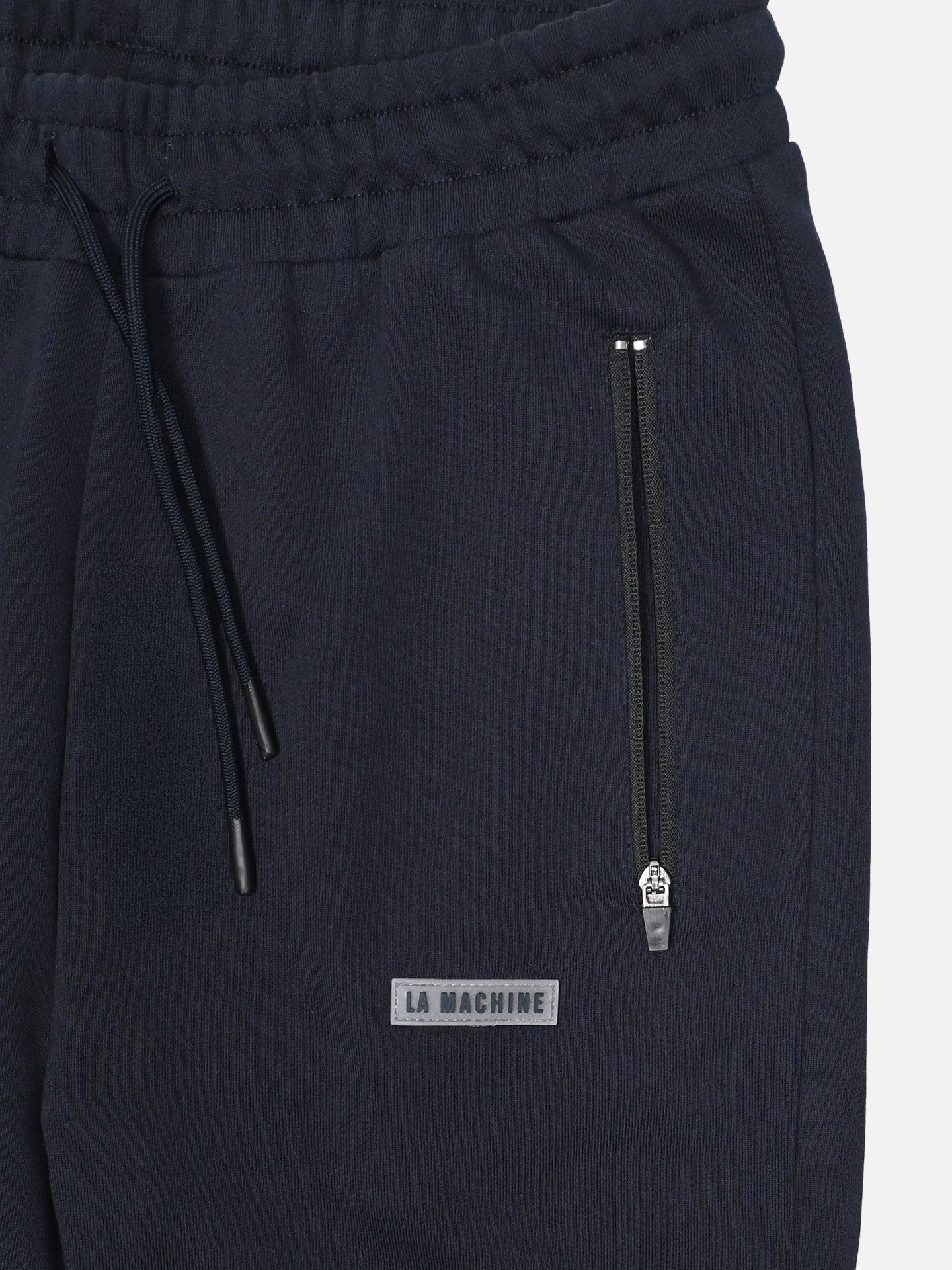 Close-up of Beyond the bike - Sweatpants in dark navy by La Machine Cycle Club, featuring an elastic waistband with drawstrings, a zippered pocket, and a small rectangular patch reading LA MACHINE.