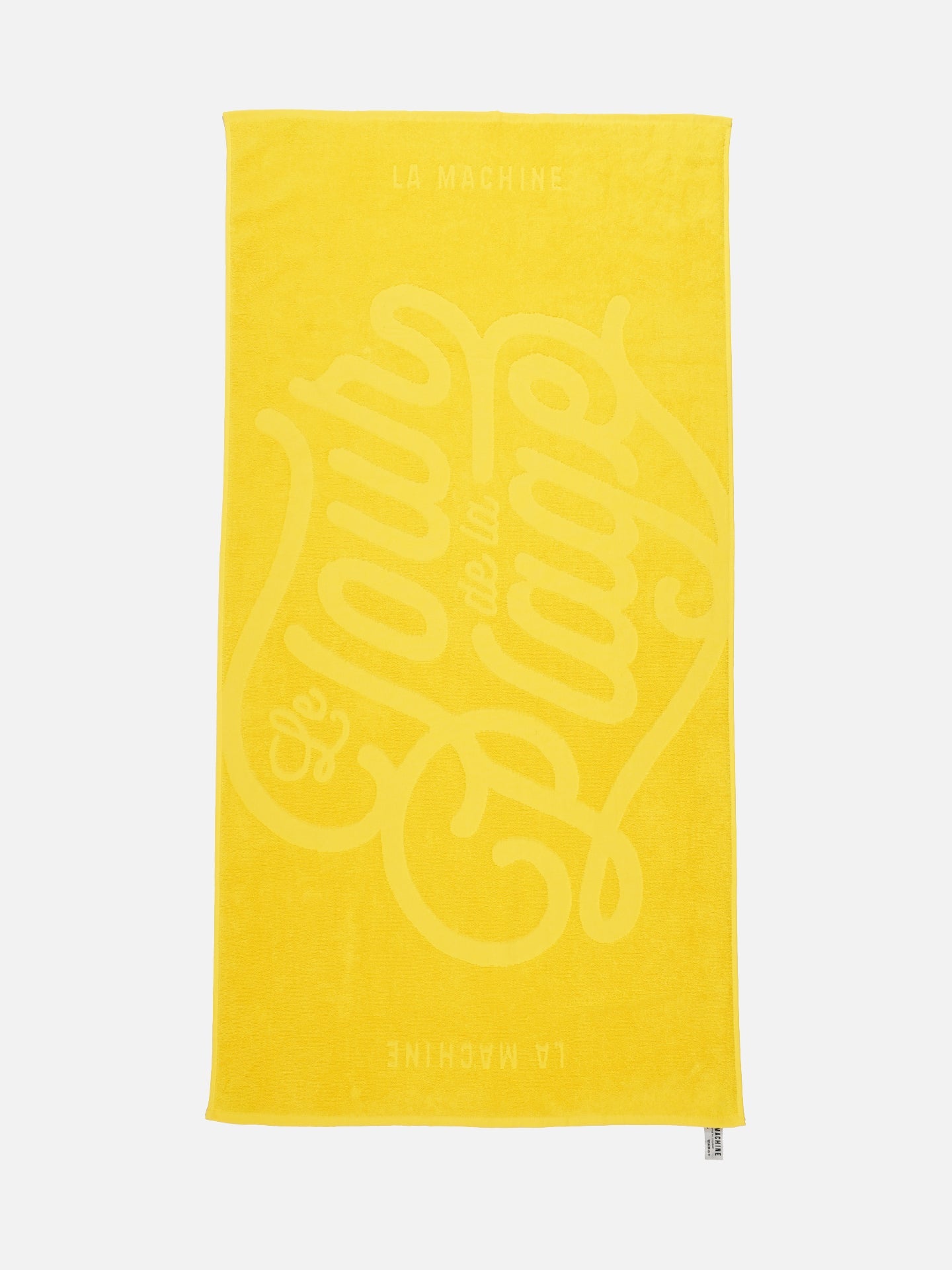 The Le Tour de la Plage - Beach Towel by La Machine Cycle Club is a bright yellow towel inspired by the yellow jersey, with Le Tour de la Plage in bold script and La Machine at the top and bottom.