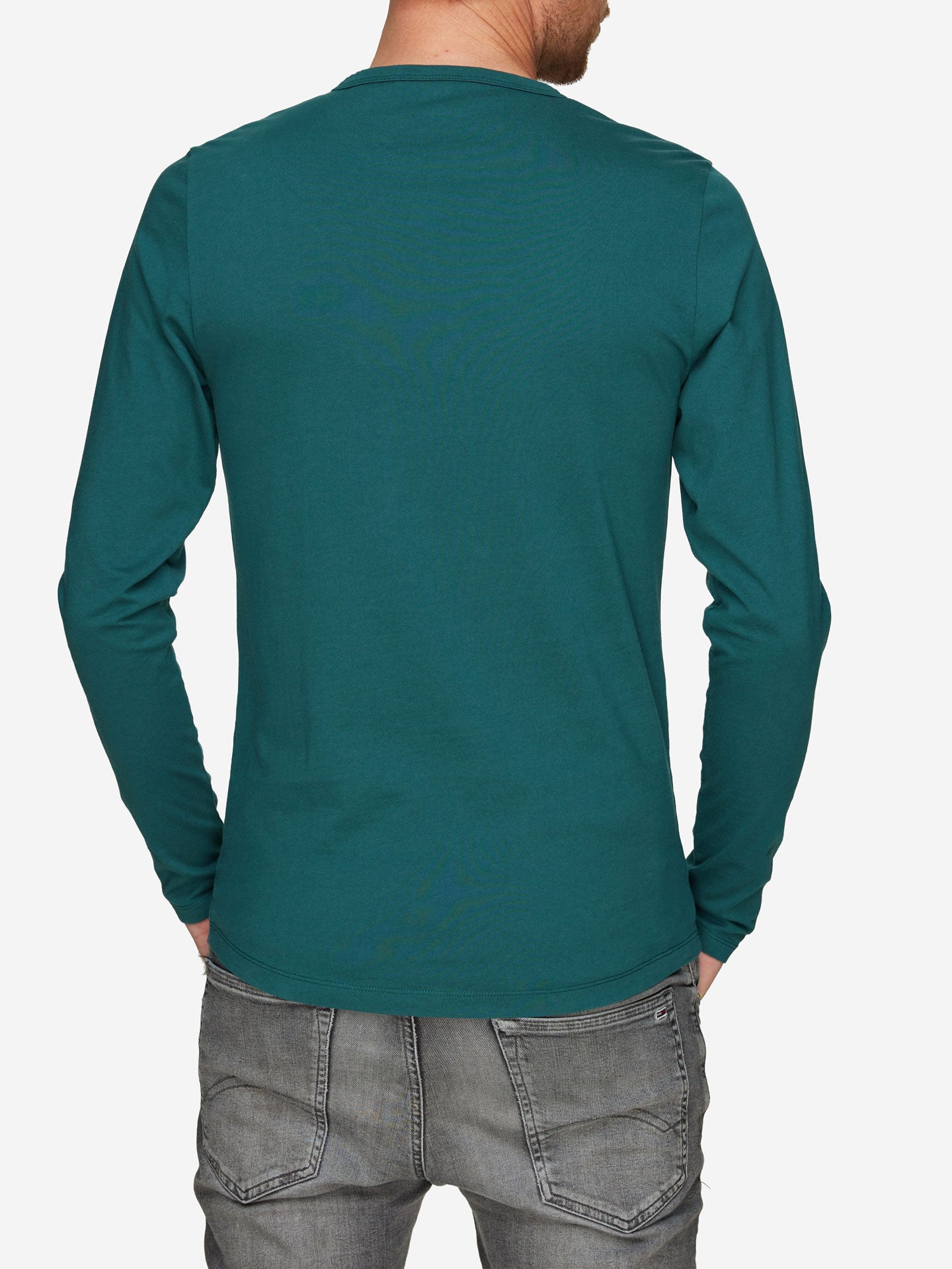 A person wearing the Pedaleur de Charme long sleeve t-shirt by La Machine Cycle Club and gray jeans, shown from the back with hands in pockets, captures casual style inspired by Hugo Koblet’s timeless charm.