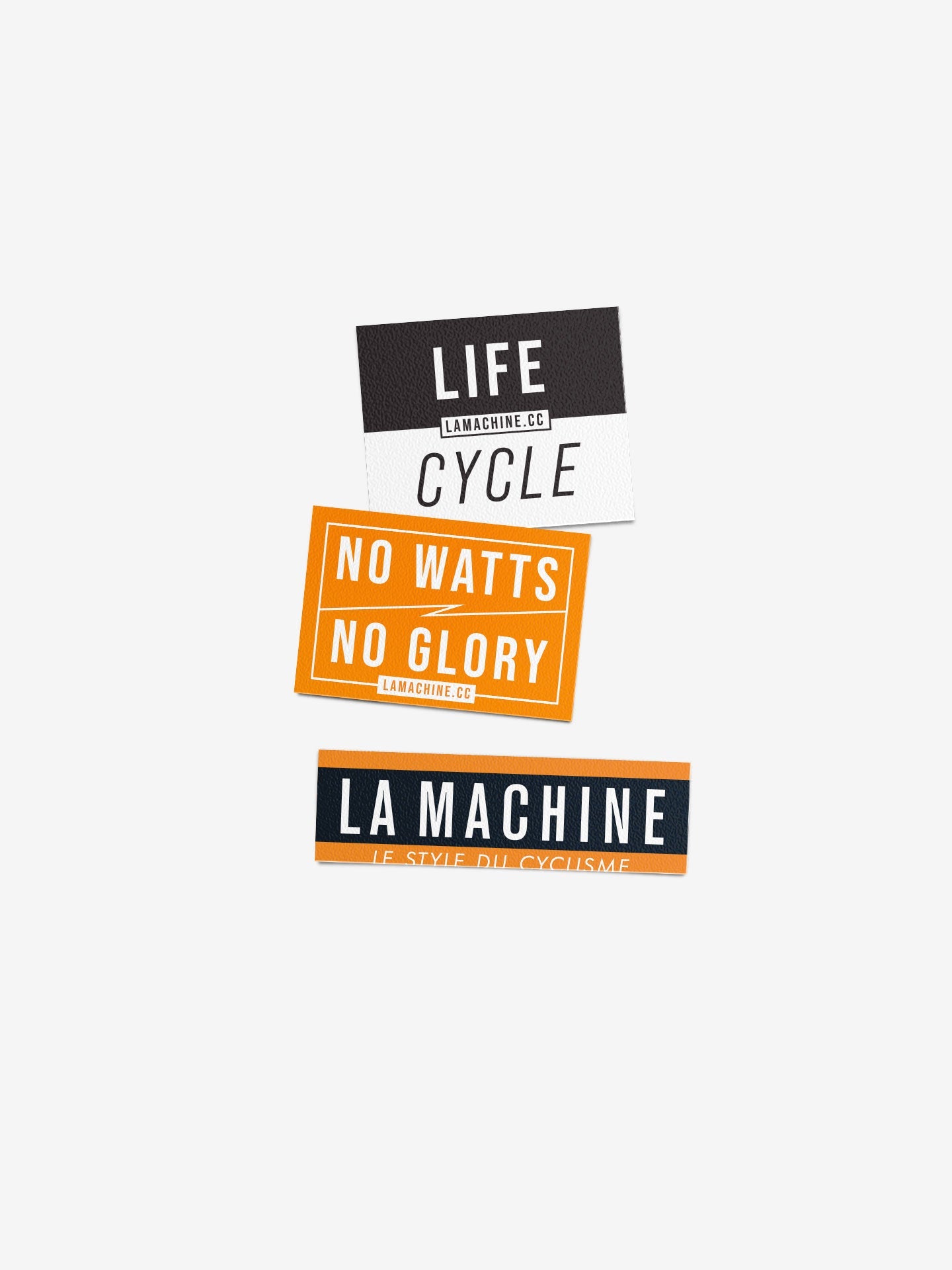 The La Machine Sticker Set - Orange & Black - 3x by La Machine Cycle Club features three durable rectangular cycling stickers: Life Cycle (black/white), No Watts No Glory (orange/white), and La Machine (orange/navy).