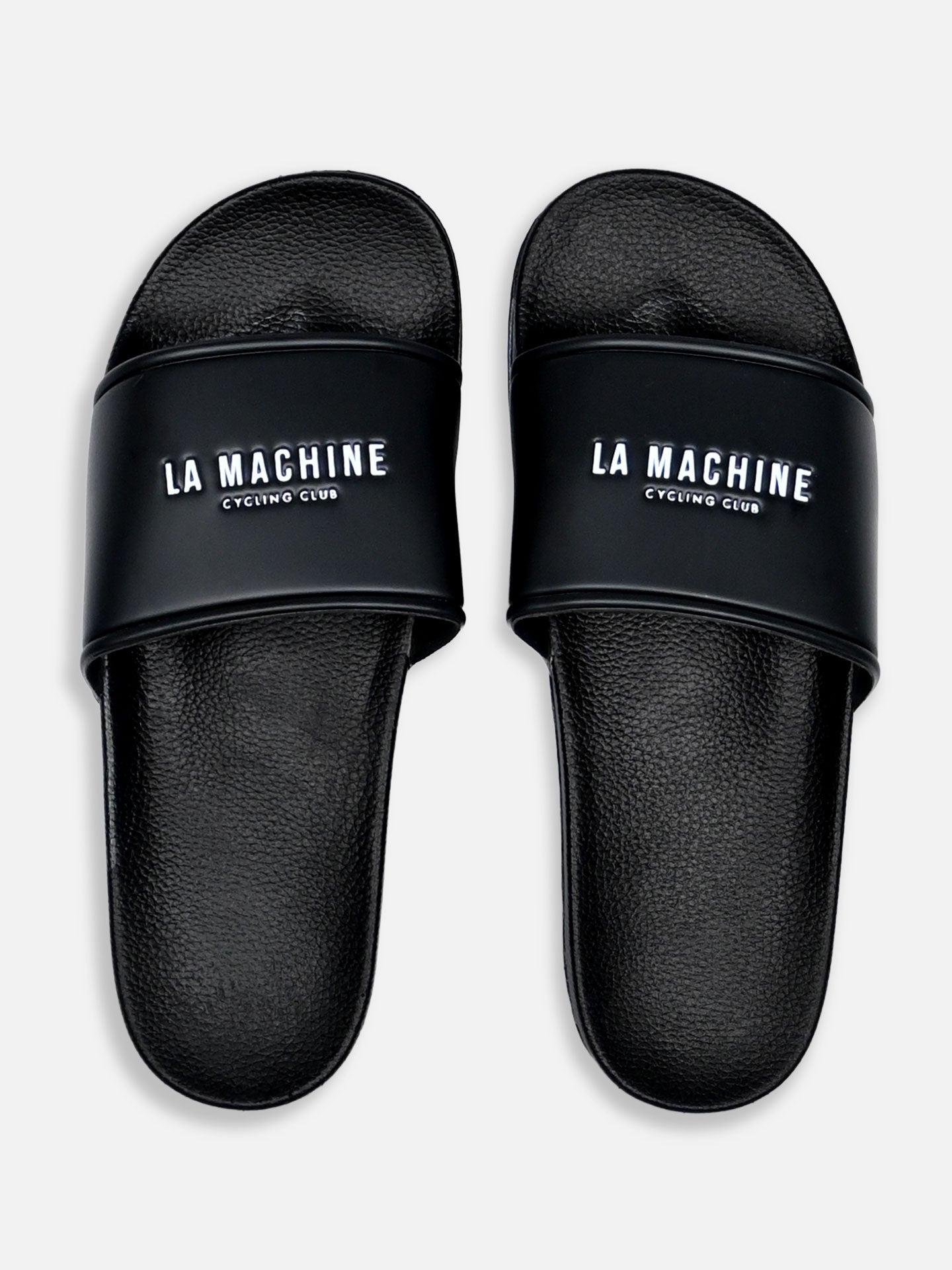 La Machine Cycle Club’s black Logo Slides feature “LA MACHINE CYCLING CLUB” in white on the straps. Seen from above on a plain background, they’re perfect as comfortable post-ride slippers.