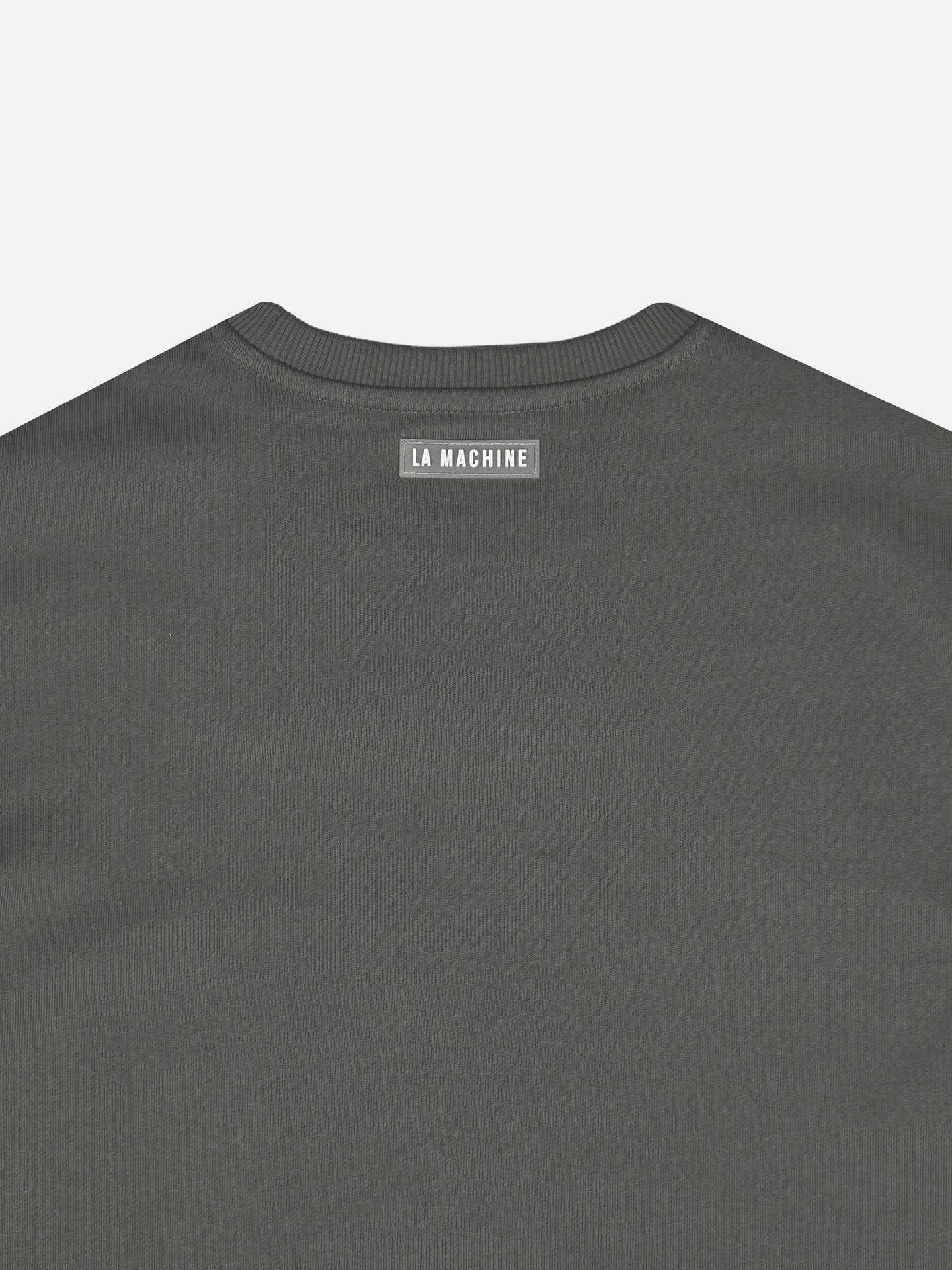 A close-up of the back of a dark grey Ride Hard Rest Hard - Sweatshirt by La Machine Cycle Club, featuring a small rectangular label near the neckline with LA MACHINE in white capital letters.