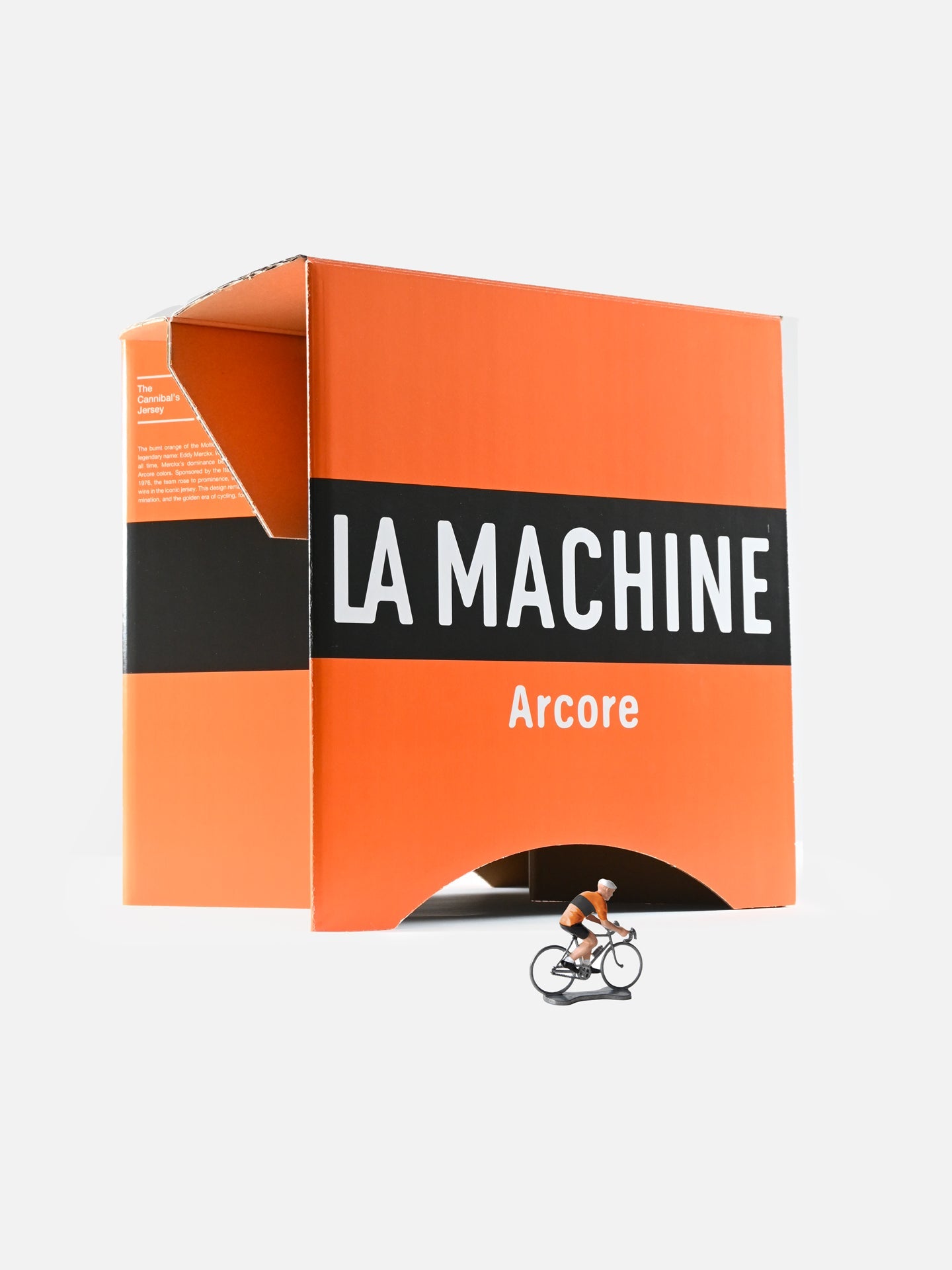 A small cyclist figurine in orange and black stands before a large LA MACHINE Arcore box—an inventive cycling tribute, just like the Molteni - 2-in-1 Stool & Sidetable by La Machine Cycle Club or other smart foldable cardboard furniture.