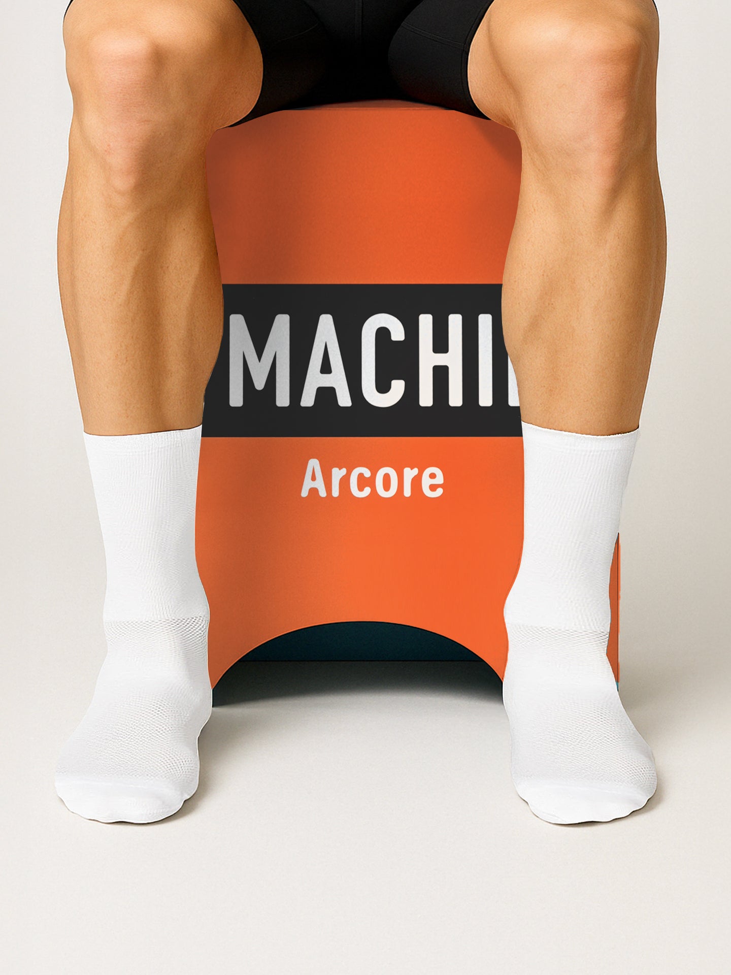A person in white socks sits on an orange Molteni - 2-in-1 Stool & Sidetable by La Machine Cycle Club, with partially visible black and white text reading MACHI and Arcore. Only their legs and lower torso are shown.