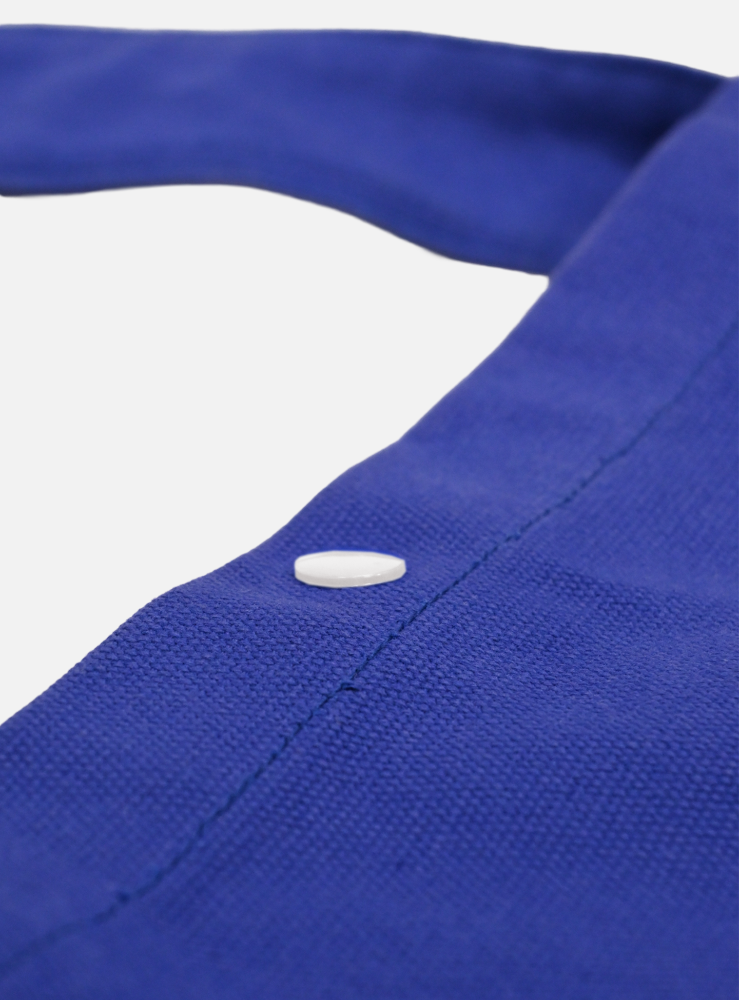 A close-up of the La Machine - Musette - Blue by La Machine Cycle Club, showing its blue fabric, visible stitching, and a single white button against a white background.