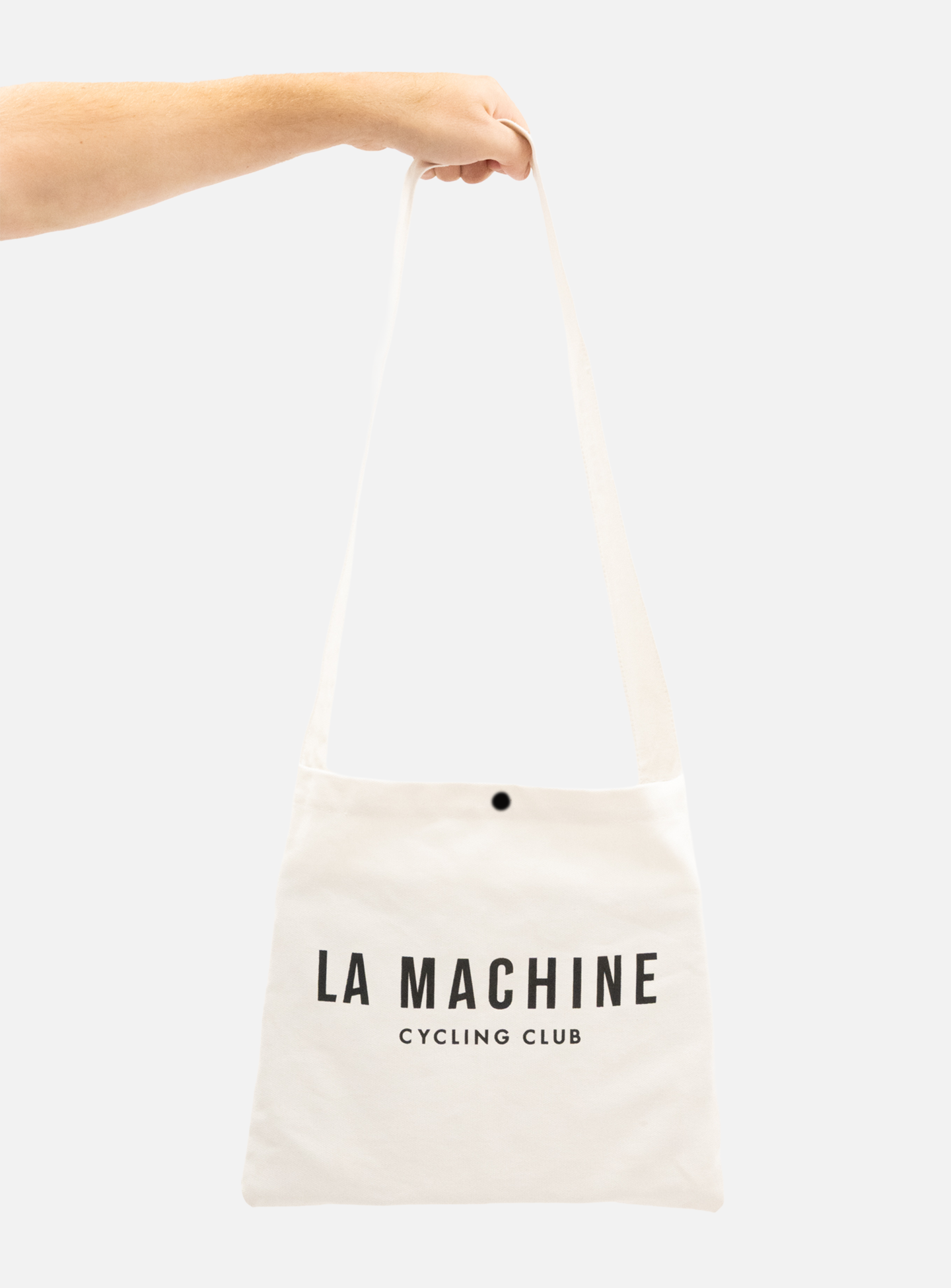 A hand holds the La Machine - Musette - White from La Machine Cycle Club, featuring bold black LA MACHINE CYCLING CLUB text on the front against a plain, light-colored background.