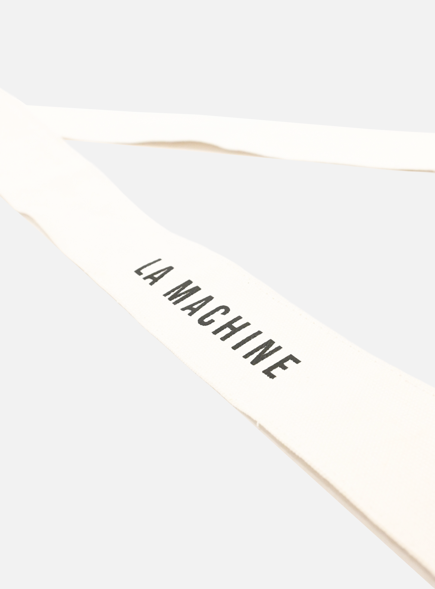 A close-up of a white fabric strap from the La Machine - Musette - White by La Machine Cycle Club, featuring “LA MACHINE” in bold black letters, set against a light background.