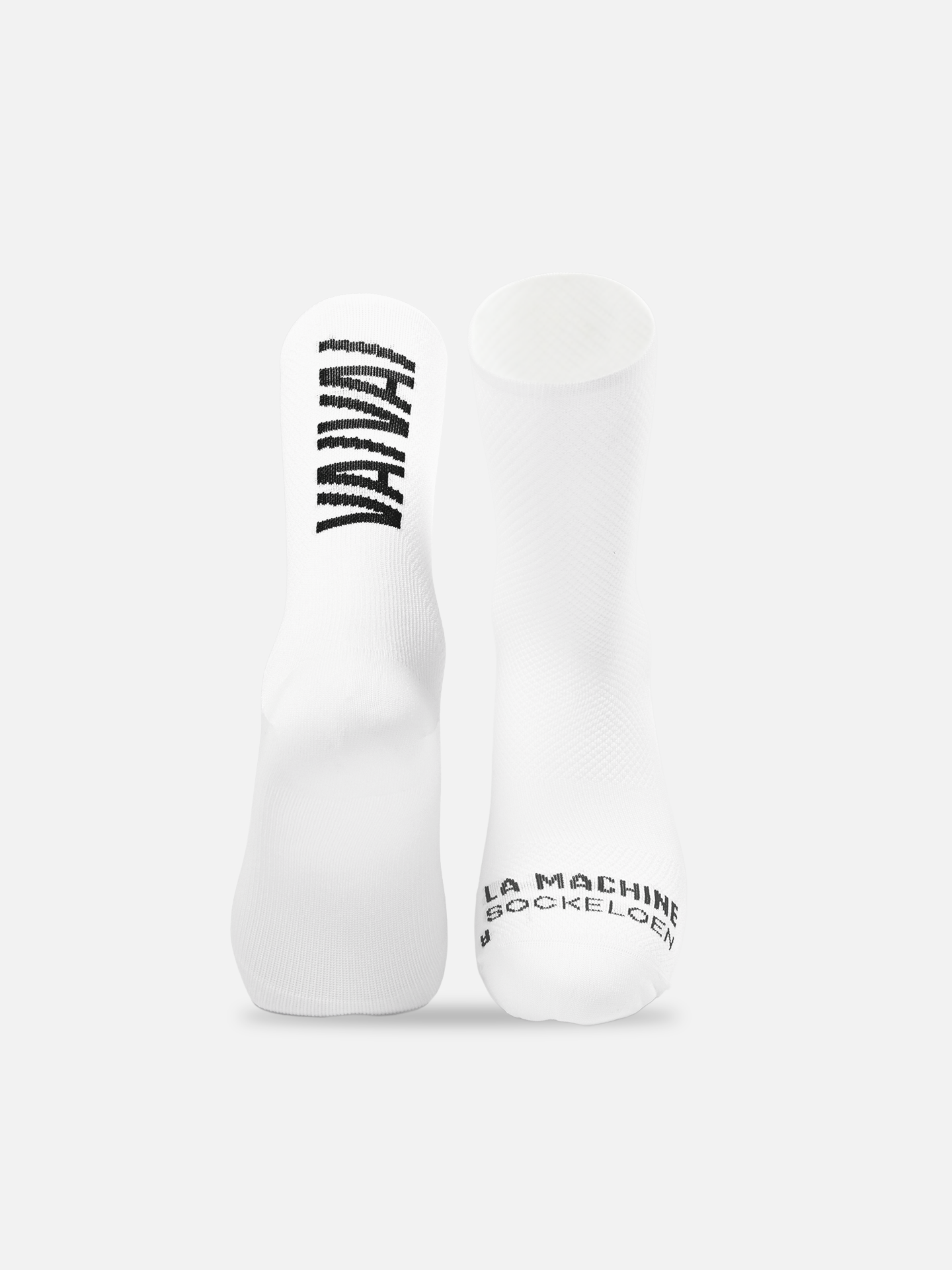 Two all-white Vai Vai Cycling Socks from La Machine Cycle Club stand upright on a white background. VANLIFE is printed boldly on the left, while the right displays LA MACHINE #SOCKDEALER near the heel; both feature seamless toes for comfort.