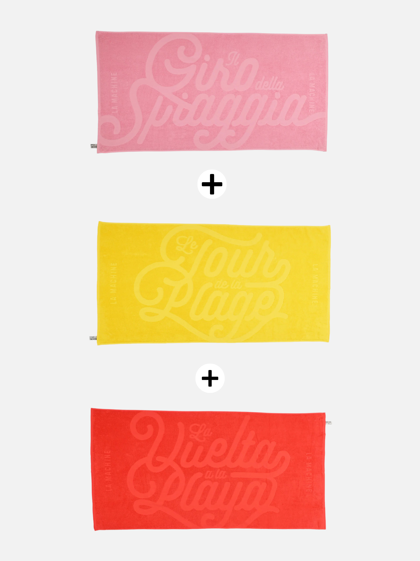 Das Grand Tours Handtuch-Bundle von La Machine umfasst drei Baumwollhandtücher — rosa mit italienischem, gelb mit französischem und rot mit spanischem Text — alle mit markanter, dekorativer Schrift, vertikal mit Pluszeichen angeordnet.